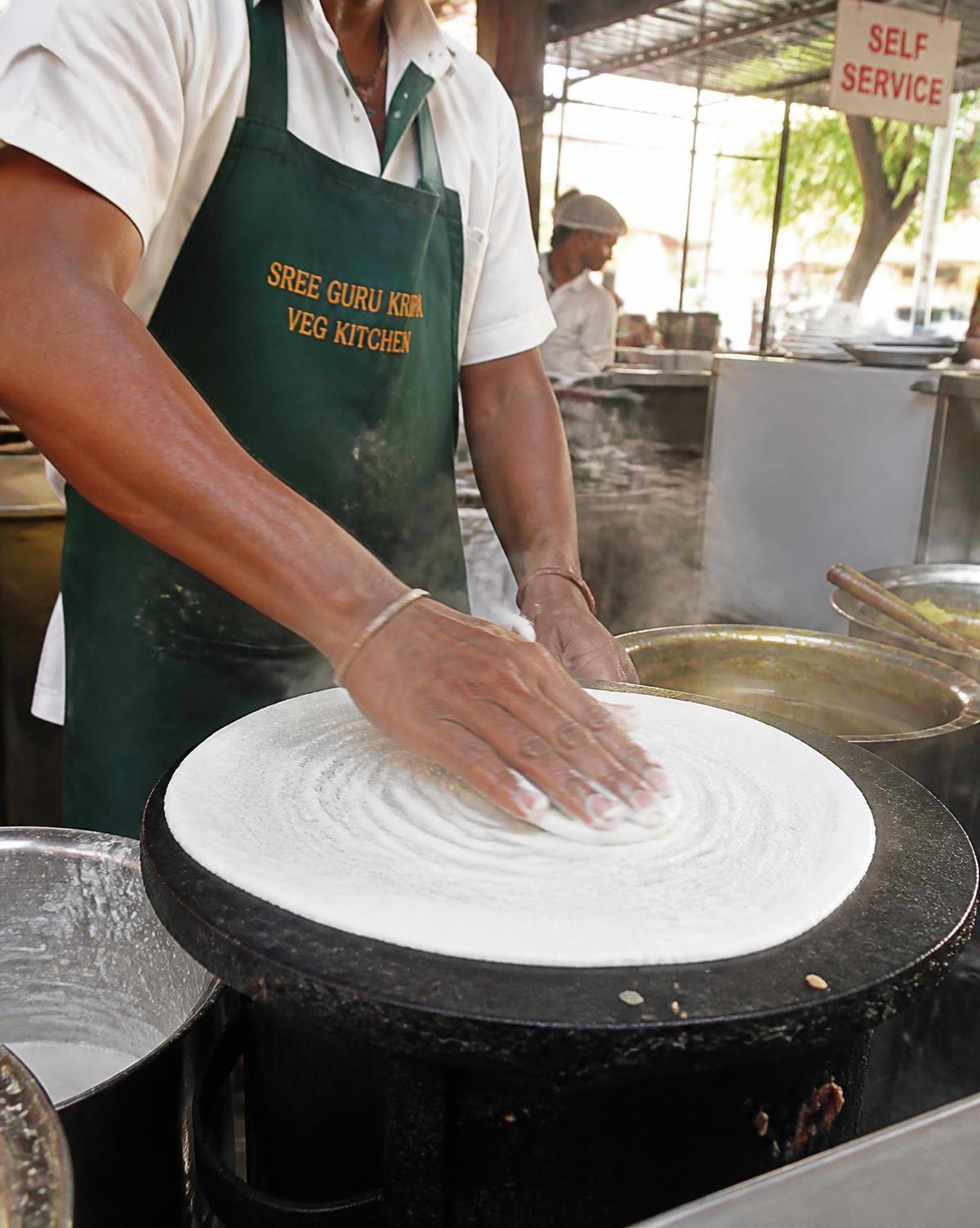 A cook spreading dosa batter on the griddle